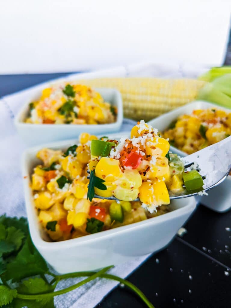 A photo of a fork holding street corn salad. with peppers, corn and cheese all in one bite.
